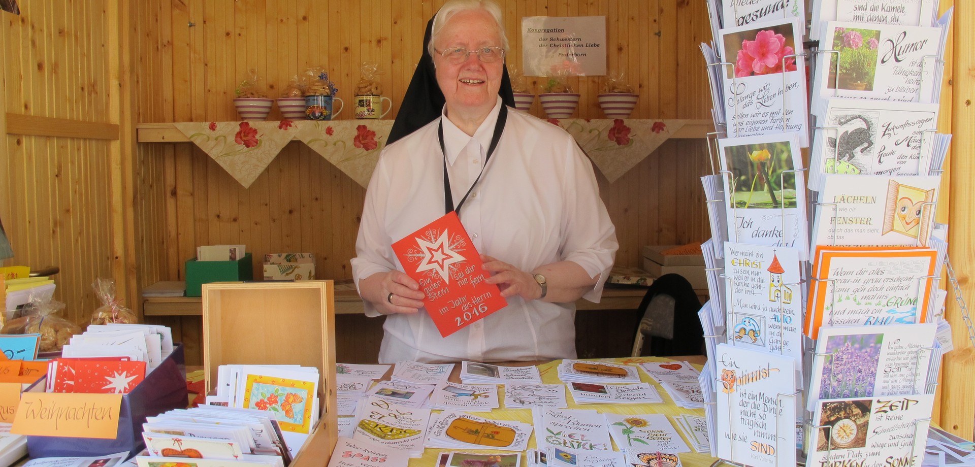 Auf dem Foto sieht man eine Ordensschwester, die am Klostermarktstand von Hand gefertigte Postkarten präsentiert.

Foto: LWL
